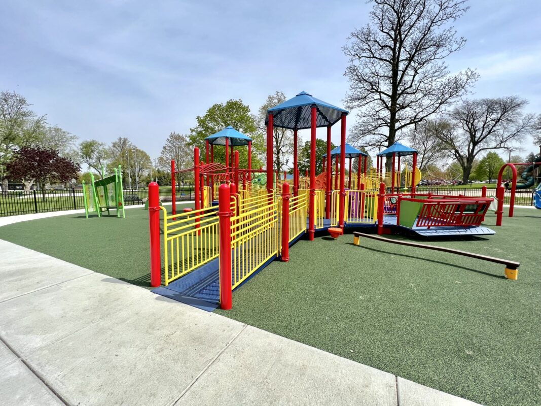 Vibrant playground with colorful equipment on green surface, surrounded by trees and blue sky, promoting joy and playfulness.