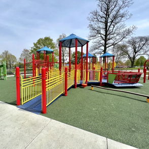 Vibrant playground with colorful equipment on green surface, surrounded by trees and blue sky, promoting joy and playfulness.