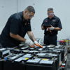 Four workers in black uniforms collaborate in a warehouse, inspecting large batteries with focus and professionalism.