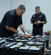 Four workers in black uniforms collaborate in a warehouse, inspecting large batteries with focus and professionalism.