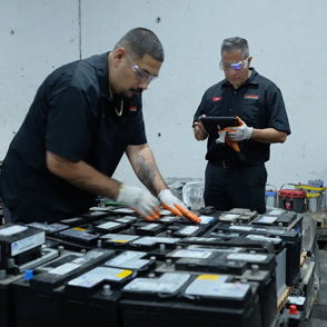 Four workers in black uniforms collaborate in a warehouse, inspecting large batteries with focus and professionalism.