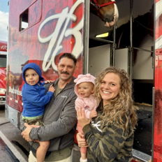 Joyful family of four smiles in front of a red truck, showcasing warmth and togetherness at a lively gathering.