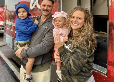 Joyful family of four smiles in front of a red truck, showcasing warmth and togetherness at a lively gathering.