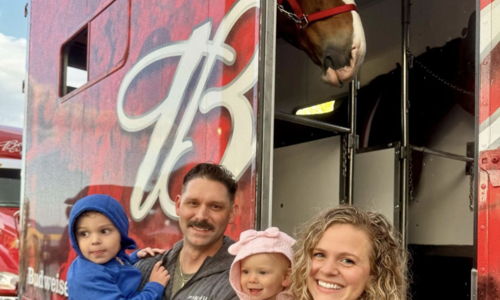 Joyful family of four smiles in front of a red truck, showcasing warmth and togetherness at a lively gathering.