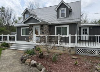 Charming house with modern and traditional elements, gray siding, stone accents, and serene landscaped yard in a peaceful setting.