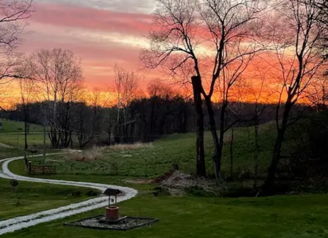 Sunset over a serene landscape with a winding path, lush green yard, and hills, evoking tranquility and reflection.