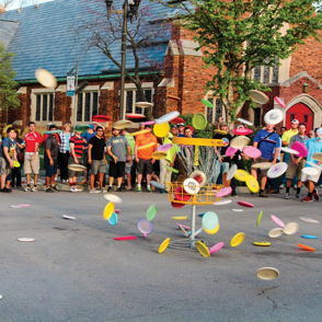 A vibrant disc golf event with flying discs, a crowd, and a charming setting exudes excitement and community spirit.