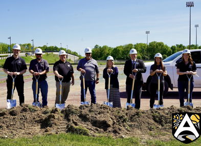 A group in hard hats holds shovels at a construction site, symbolizing unity and excitement for a new community project.