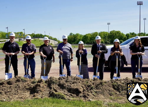 A group in hard hats holds shovels at a construction site, symbolizing unity and excitement for a new community project.