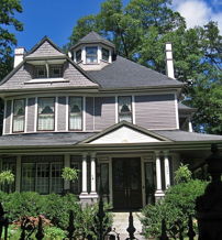 Charming two-story house with turret, steep roof, and large windows, surrounded by gardens, evoking nostalgia and tranquility.