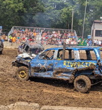 Demolition derby scene with damaged cars in a muddy arena, crowd excitedly watching the thrilling competition.