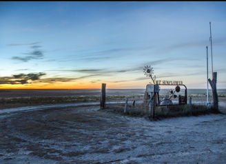 Desolate landscape with a winding path, rustic structure, and a serene sunset evoking nostalgia and introspection.