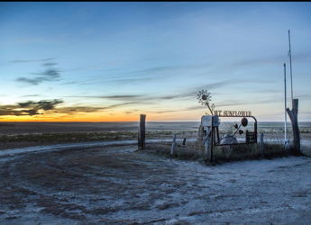 Desolate landscape with a winding path, rustic structure, and a serene sunset evoking nostalgia and introspection.