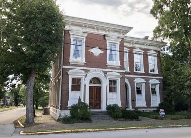 Elegant two-story brick house with large windows, surrounded by greenery, exudes warmth, nostalgia, and a welcoming presence.