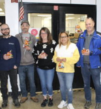 A cheerful group of eight in casual attire shares a light moment in a workplace, enjoying snacks and camaraderie.