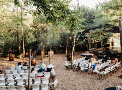 A serene outdoor event setting with white chairs, guests seated, and a stage area, evoking a calm, romantic atmosphere.