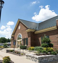 A welcoming brick building with landscaping, a paved path, and a bright sky, suggesting community and warmth.
