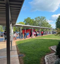 People wait outside a building on a sunny day, creating a sense of anticipation and community.