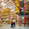 Warehouse scene with shelves of boxes, two workers discussing, bright colors, evoking productivity and teamwork in logistics.