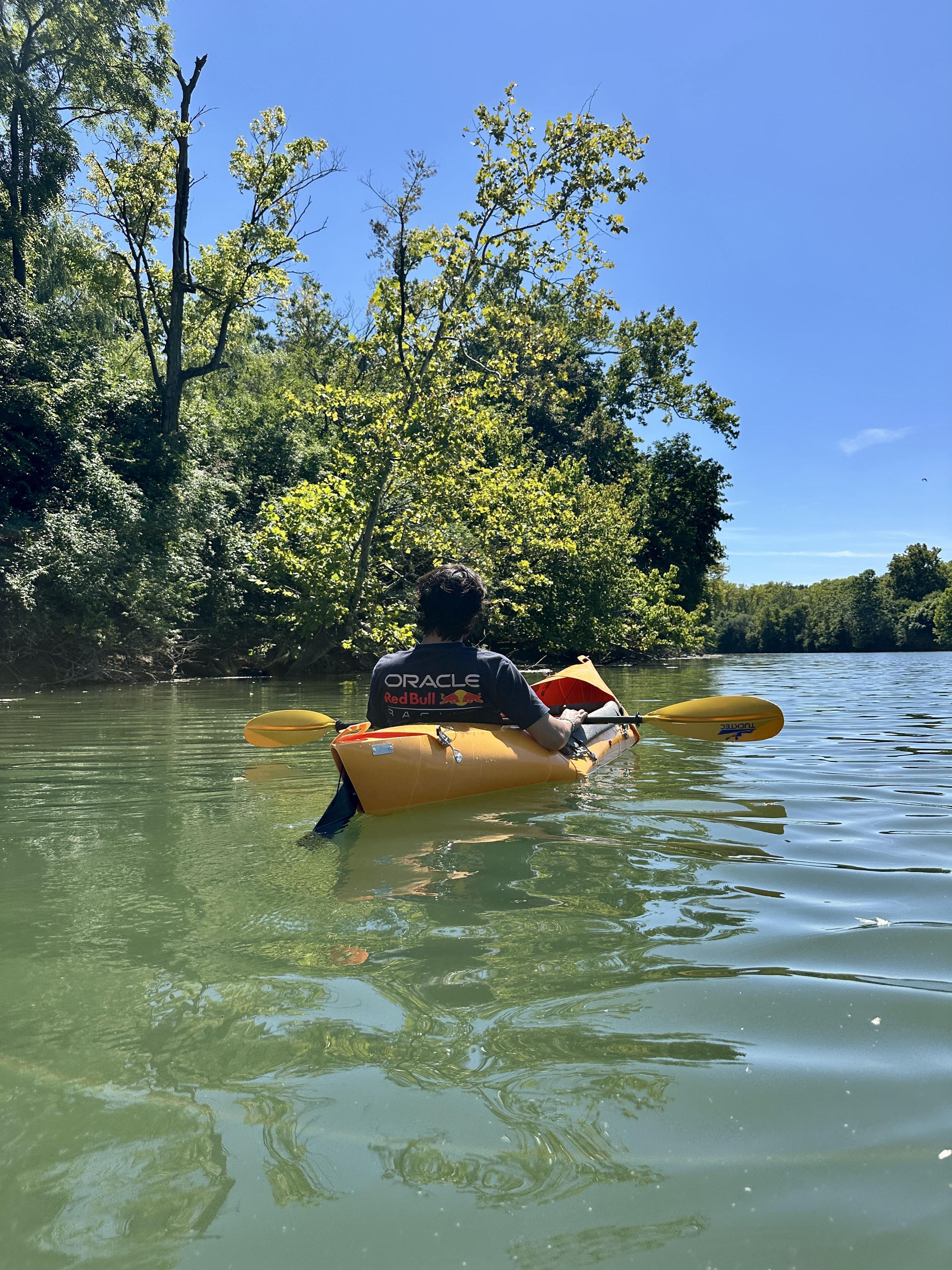 A person kayaks on calm water, surrounded by lush greenery and blue skies, evoking peace, adventure, and joy in nature.