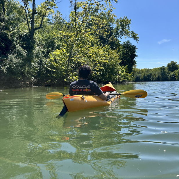 A person kayaks on calm water, surrounded by lush greenery and blue skies, evoking peace, adventure, and joy in nature.
