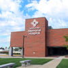 Modern Memorial Hospital with brick exterior, green pathways, trees, and a clear sky, evokes care, safety, and hope.