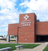 Modern Memorial Hospital with brick exterior, green pathways, trees, and a clear sky, evokes care, safety, and hope.