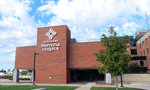 Modern Memorial Hospital with brick exterior, green pathways, trees, and a clear sky, evokes care, safety, and hope.