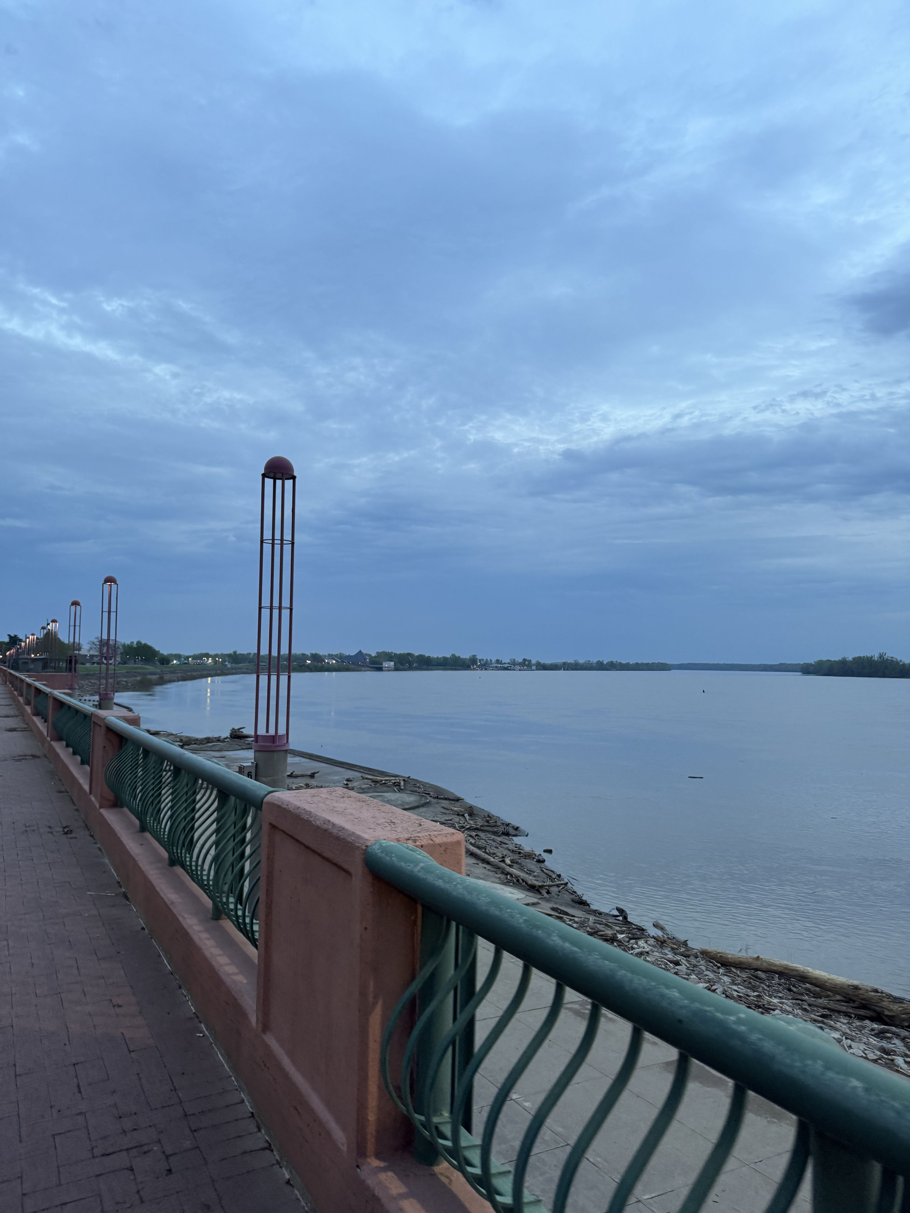 A peaceful waterfront scene with a railing, calm water, and a cloudy sky, evoking tranquility and reflection.