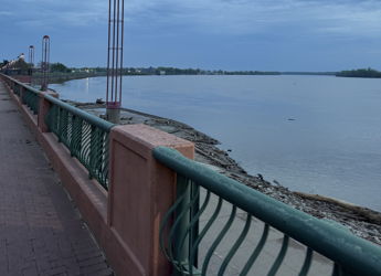 A peaceful waterfront scene with a railing, calm water, and a cloudy sky, evoking tranquility and reflection.