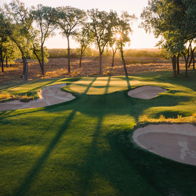 A serene golf course at sunset with sand traps, greens, and tall trees, radiating tranquility and connection to nature.