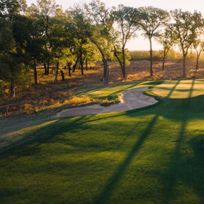 A serene golf course at sunset with sand traps, greens, and tall trees, radiating tranquility and connection to nature.