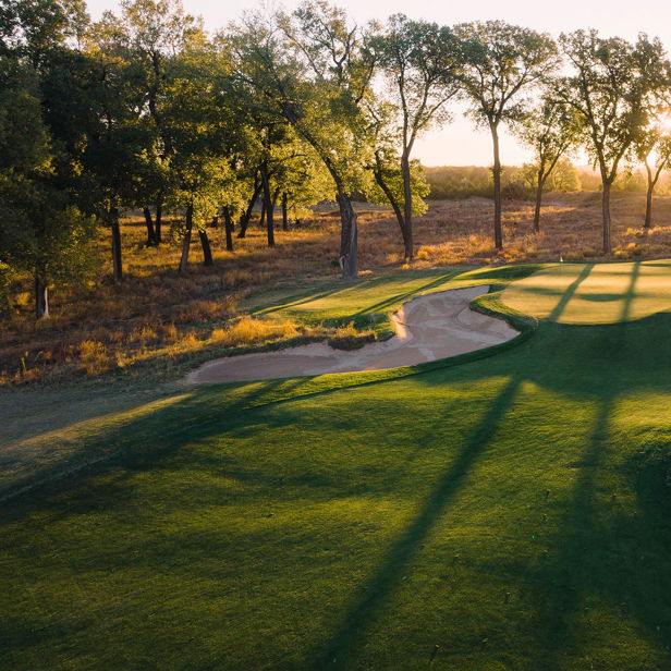 A serene golf course at sunset with sand traps, greens, and tall trees, radiating tranquility and connection to nature.