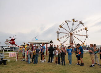 A lively fair scene with families near a Ferris wheel, evoking joy, excitement, and a sense of community.