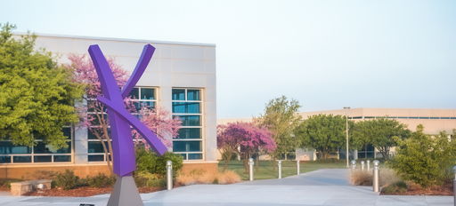 Modern outdoor scene with a vibrant purple sculpture, blooming pink trees, and a contemporary building, evoking calm and inspiration.