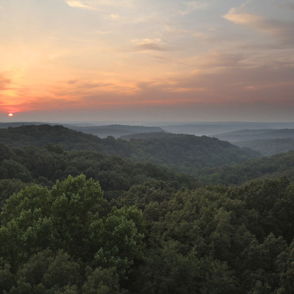 Serene sunset landscape with rolling hills, warm hues, and mist, evoking calmness and reflection in nature's beauty.