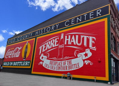 A six-pack of Coca-Cola bottles in a red carrier, celebrating the brand's history and evoking nostalgia and joy.