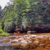 A serene river scene with a person in a red kayak paddling through lush greenery and rocks, evokes peace and adventure.