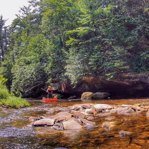 A serene river scene with a person in a red kayak paddling through lush greenery and rocks, evokes peace and adventure.