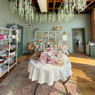 Charming shop interior with greenery, soft colors, rustic beams, and a welcoming table, evoking warmth and creativity.
