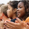 A joyful group of children in orange shirts cheer together, exuding excitement and community spirit in a festive atmosphere.