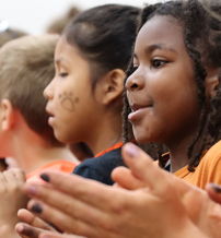 A joyful group of children in orange shirts cheer together, exuding excitement and community spirit in a festive atmosphere.