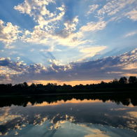 A tranquil landscape with water reflecting a vibrant dawn/dusk sky filled with soft hues of orange, blue, and white.