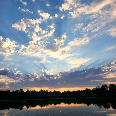 A tranquil landscape with water reflecting a vibrant dawn/dusk sky filled with soft hues of orange, blue, and white.