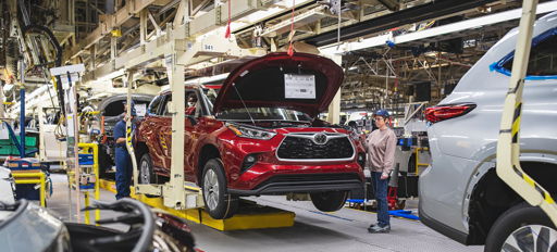 A busy automotive assembly line with a red car being inspected, showcasing worker focus and the energy of modern production.