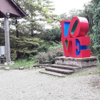 Colorful "LOVE" sculpture in red and blue surrounded by greenery, creating a joyful and peaceful atmosphere.