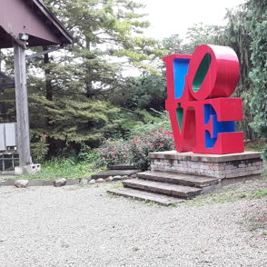 Colorful "LOVE" sculpture in red and blue surrounded by greenery, creating a joyful and peaceful atmosphere.