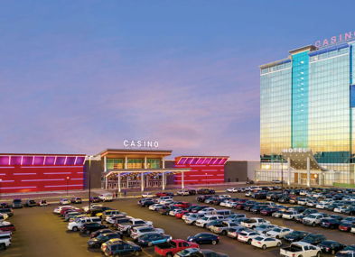 A vibrant casino and hotel with colorful lights and a busy parking lot, set against a serene dawn or dusk sky.