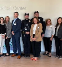 A diverse group in professional attire smiles together at Aurora Medical Center, suggesting teamwork and collaboration.
