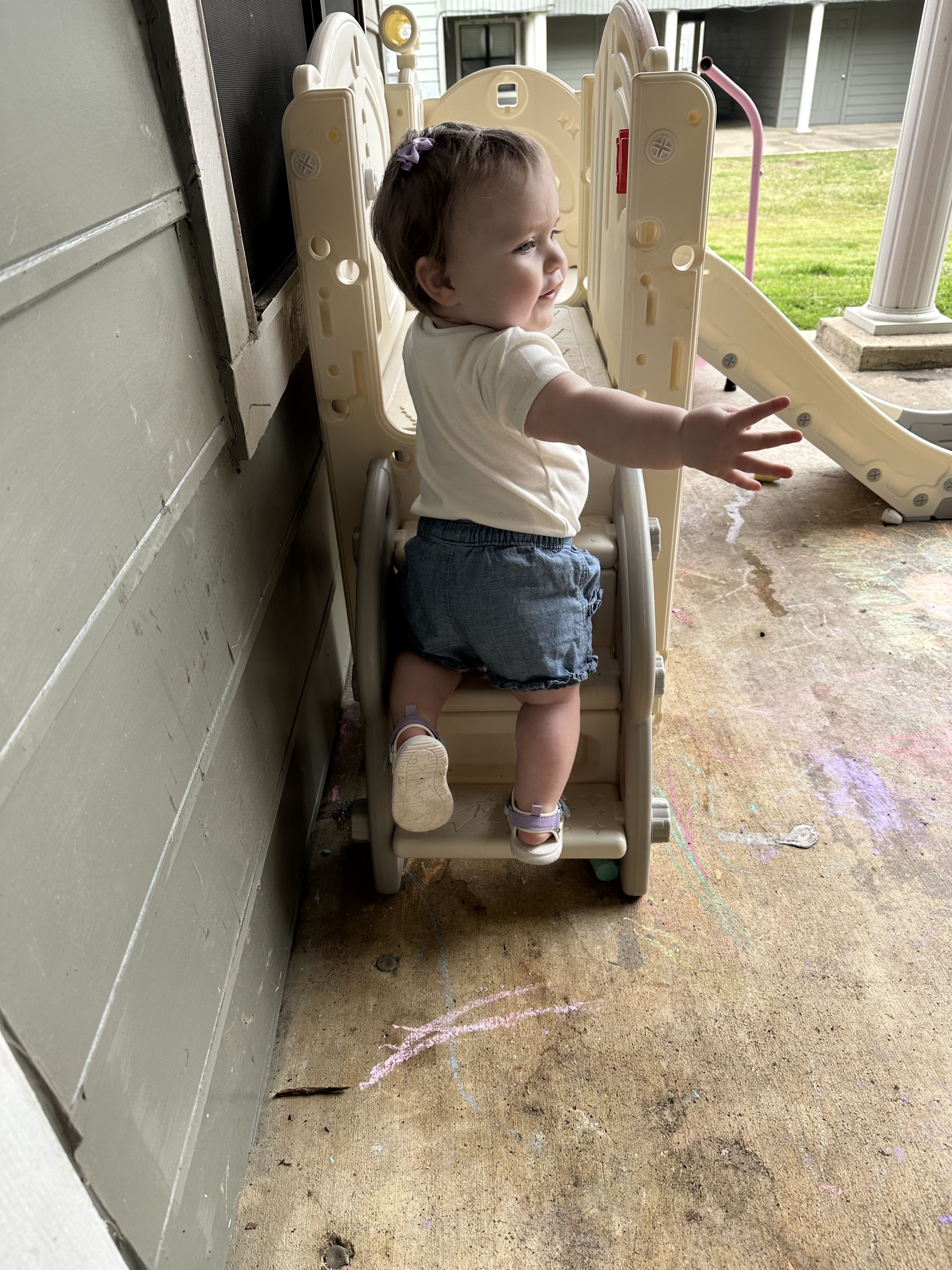 Child at the top of a slide in a playful backyard, arms outstretched, radiating joy and curiosity of childhood.